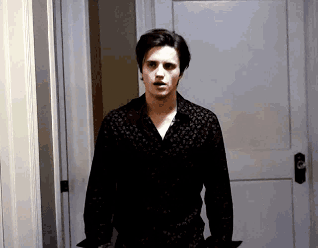 a man in a black shirt is standing in front of a white door