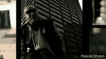 a man is sitting in front of a tall building wearing sunglasses and a necklace .
