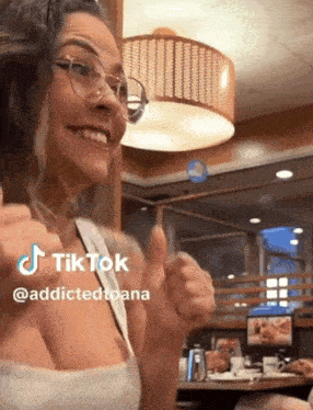 a woman wearing glasses is giving a thumbs up in a restaurant .