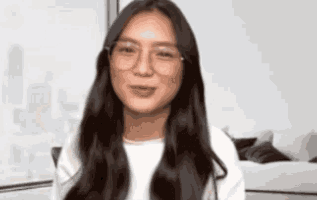 a woman wearing glasses and a white shirt is sitting in front of a window .