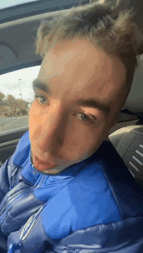 a young man wearing a blue jacket is sitting in the back seat of a car