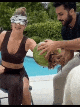 a man and a woman are playing with a watermelon by the pool .