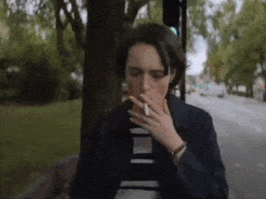 a woman in a blue jacket is smoking a cigarette on the side of the road .