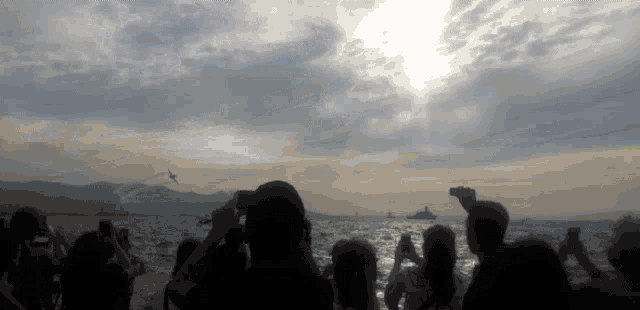 a group of people taking pictures of a plane flying over the water