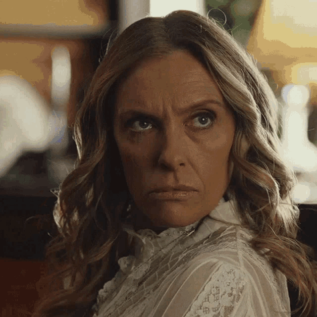 a woman with a serious look on her face wearing a white lace top