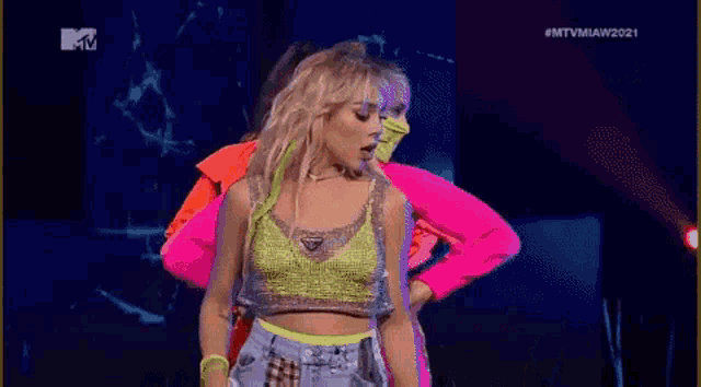 a group of women are dancing on a stage in neon clothes .