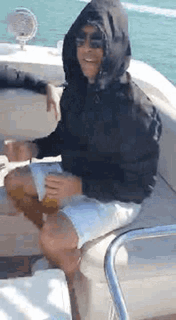 a man wearing a hooded jacket and sunglasses is sitting on a boat .