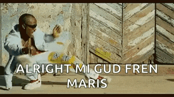 a man is sitting on the ground in front of a wooden wall with the words `` alright mi gud fren maris '' above him .