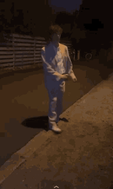a person in a white suit walking down a sidewalk at night