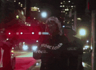a person wearing a chrome hearts sweatshirt is walking down a street at night