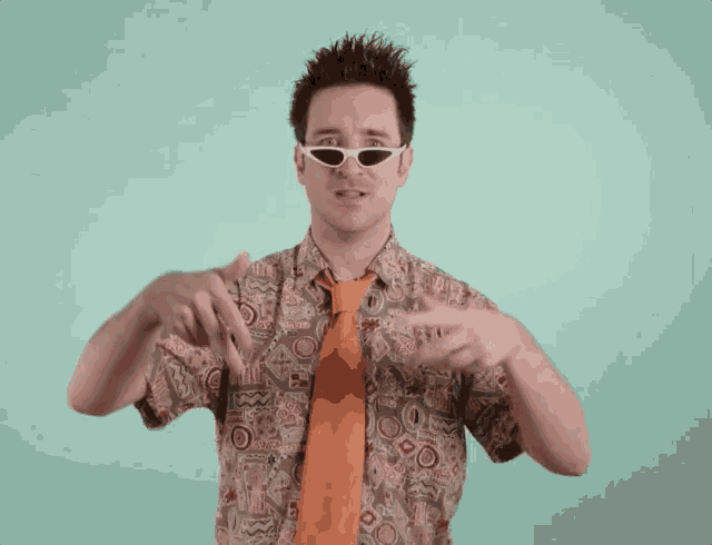 a man wearing sunglasses and an orange tie is pointing at something