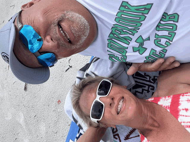 a man and a woman are laying on the beach and the man is wearing a shirt that says oakbrook