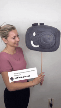 a woman in a pink shirt is holding a camera on a stick with a reply to abbaxpokemon154 's comment