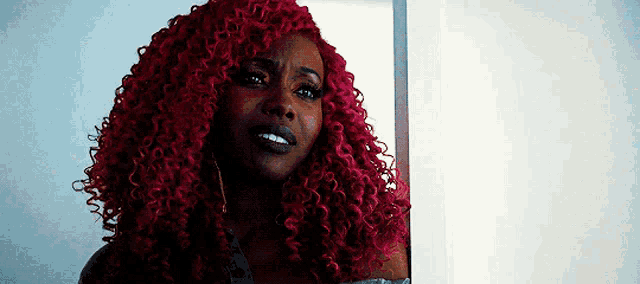 a woman with red curly hair is standing in front of a window .