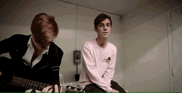 a man wearing a pink shirt that says i love you is playing a guitar