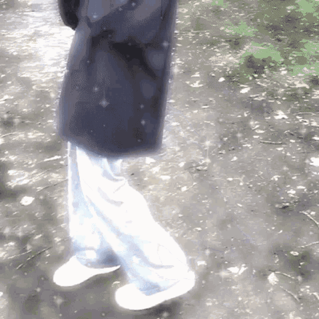 a person wearing a black coat and white pants is walking on a path .