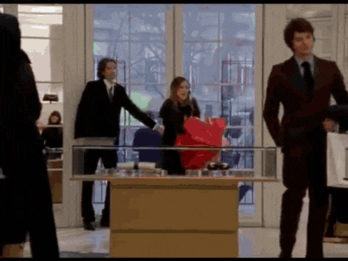 a man in a suit stands next to a woman holding a red bag in a store
