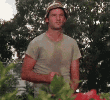 a man wearing a hat and a t-shirt is standing in front of some flowers .