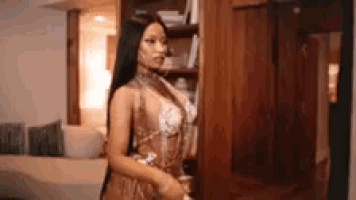 a woman in a sheer dress is standing in a room next to a bookshelf .