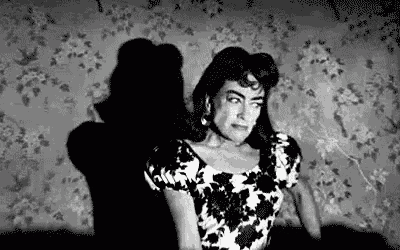 a black and white photo of a woman sitting in a chair in front of a wall with flowers on it .