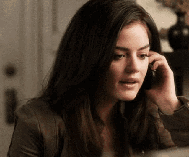 a woman is talking on a cell phone while sitting at a table in a room .