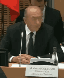 a man in a suit and tie is sitting at a table with a name plate that says m. gerard collomb