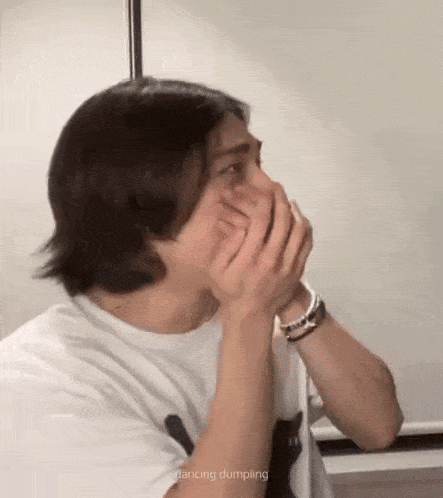 a man is covering his mouth with his hands while wearing a white shirt .