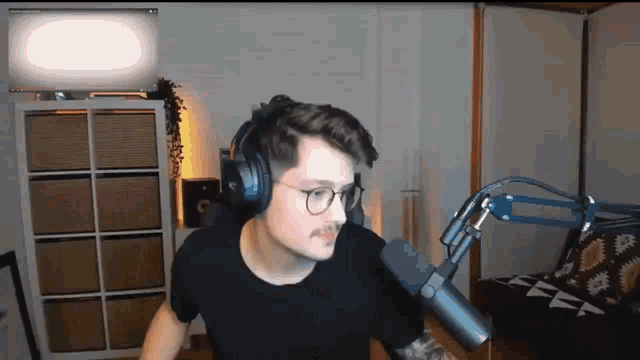 a man with glasses and headphones is standing in front of a microphone .