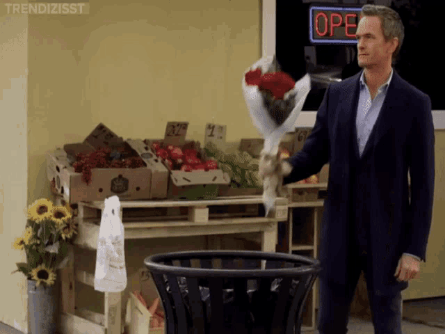 a man throws a bouquet of roses into a trash can in front of a store that is open