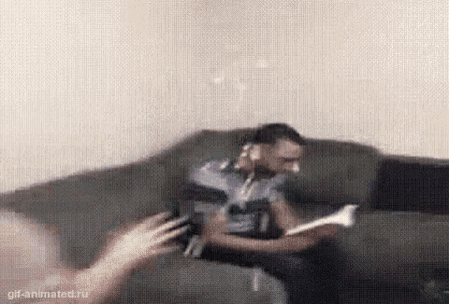 a man is sitting on a couch reading a book and smoking a pipe .