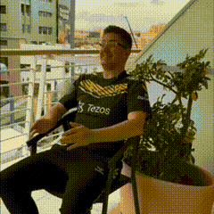 a man is sitting in a chair on a balcony with a tezos shirt on