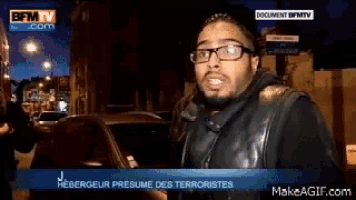 a man wearing glasses and a leather vest is standing in front of a car