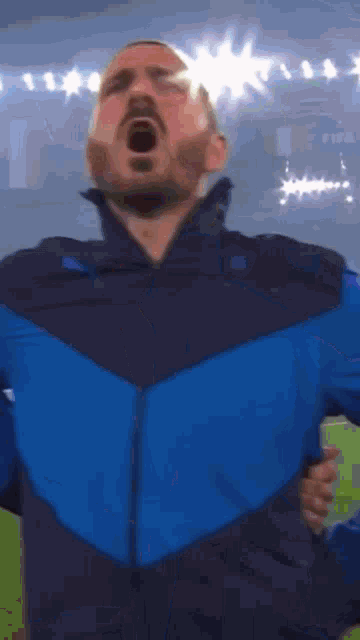a man in a blue jacket is standing on a field with his mouth open .