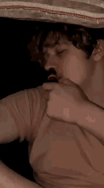a young man with curly hair is smoking an electronic cigarette under a bed .