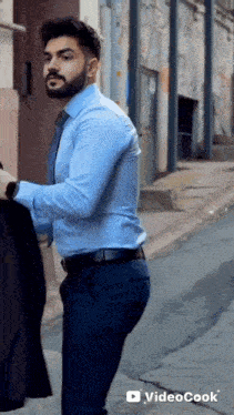 a man with a beard wearing a blue shirt and tie is standing on a street .