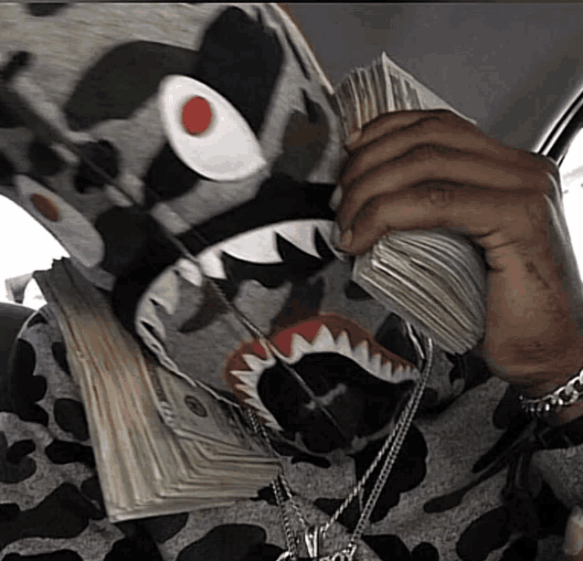 a person wearing a shark mask is holding a stack of money in front of their face