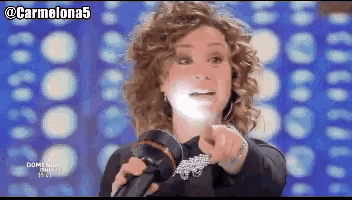 a woman with curly hair is holding a hair dryer and pointing at the camera