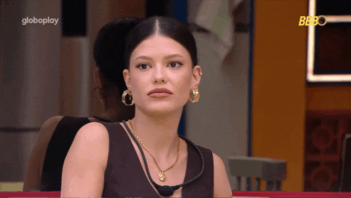 a woman wearing a necklace and hoop earrings is sitting in front of a globeplay sign