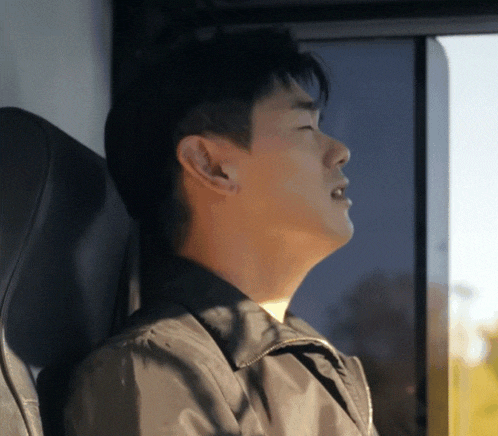 a man in a black jacket looks out a window with his eyes closed