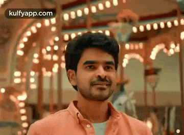a man in an orange shirt is standing in front of a merry go round .