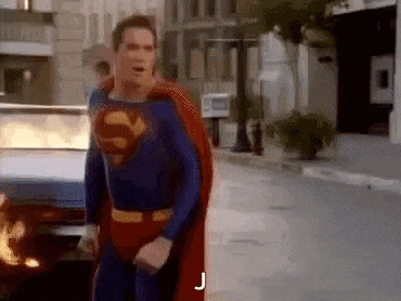 a man in a superman costume is walking down a street next to a burning car .
