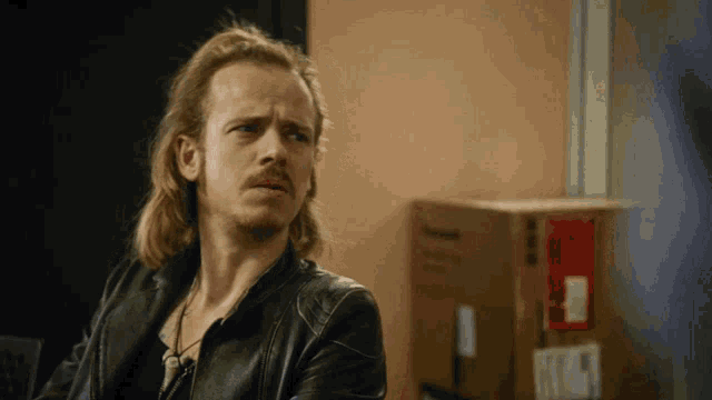 a man with long hair and a beard wearing a black jacket