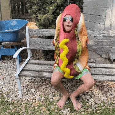 a boy dressed as a hot dog with mustard on it sits on a bench