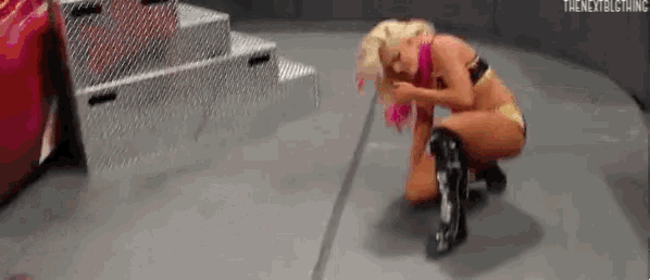 a female wrestler is kneeling down on the floor in a wrestling ring .