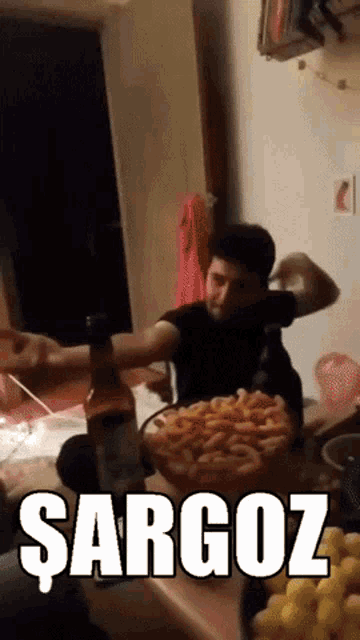 a man sitting at a table with a bowl of french fries and a bottle of wine that says sargoz