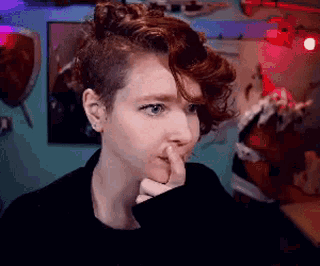 a woman with a shaved head holds her finger to her mouth