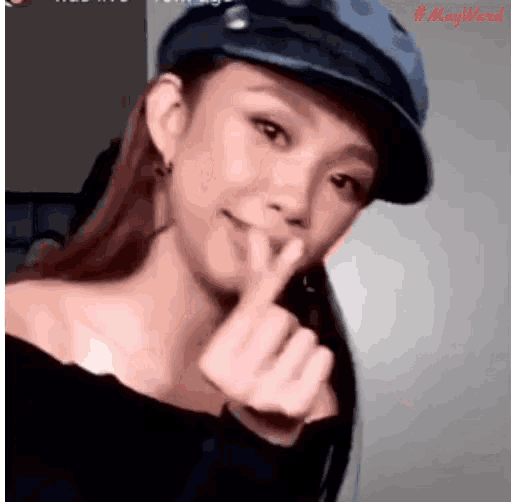a woman wearing a blue hat is making a heart with her finger