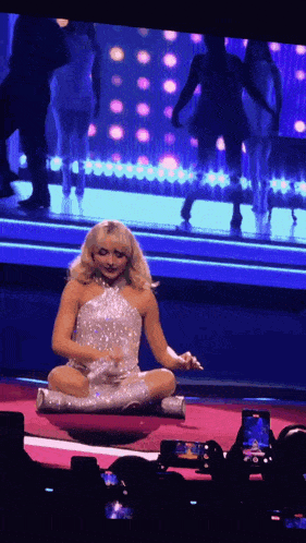 a woman in a silver dress is sitting on a stage in front of a crowd