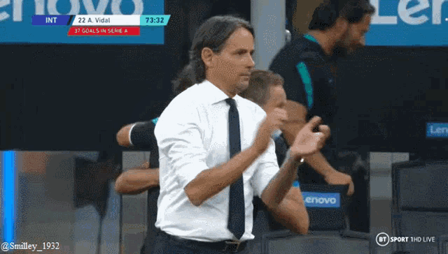 a man in a white shirt and tie applauds in front of a screen that says lenovo
