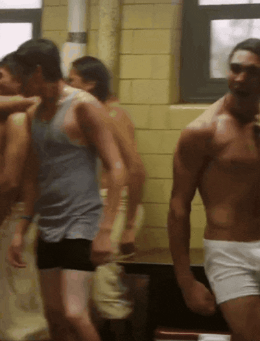 a group of shirtless men are standing in a room with a window